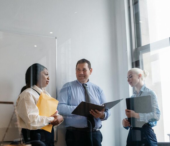 Behördliche Mitarbeiter in einem Büro tragen Unterlagen und unterhalten sich freundlich.